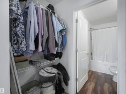 Built-in wired shelving system, wood-finish flooring, white paneled door, and a full bathtub with shower - 