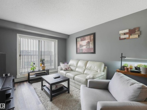 Spacious living area featuring wood-finish flooring, neutral gray wall tones, and a large sliding glass door - #414 340 Windermere Rd Nw, Edmonton, AB 