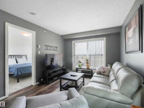 Wood-finish flooring, sliding glass door, white vertical blinds, and a bedroom with carpet - #414 340 Windermere Rd Nw, Edmonton, AB 