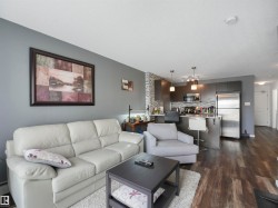 Open-concept living space featuring wood-finish flooring, a modern kitchen with stainless steel appliances, and a tiled kitchen backsplash - 