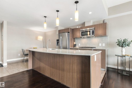 Curved kitchen island with an undermount sink, wood-finish cabinetry, stainless steel appliances, and pendant lighting - #416 2510 109 St Nw, Edmonton, AB 