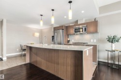 Curved kitchen island with an undermount sink, wood-finish cabinetry, stainless steel appliances, and pendant lighting - 