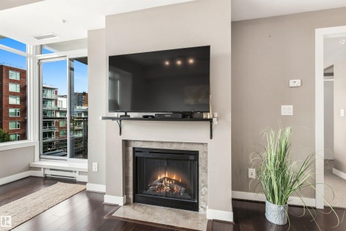 Built-in fireplace with stone surround, dark wood-finish flooring, and expansive windows - #416 2510 109 St Nw, Edmonton, AB 