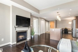 Open-concept living area featuring a fireplace with stone surround, wood-finish flooring, a kitchen island with built-in sink, and pendant lighting - 
