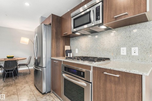 Stainless steel appliances, wood-finish cabinetry, speckled countertop, tiled flooring, and a full backsplash - #416 2510 109 St Nw, Edmonton, AB 