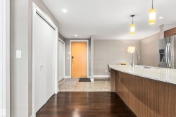 Dark wood-finish flooring, white bi-fold closet doors, light-toned entryway tile, curved island with a light-colored countertop, and a stainless steel refrigerator - 