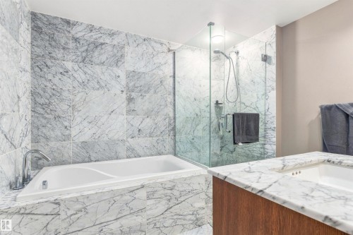 White soaking tub, glass-enclosed shower, stone tile walls, stone countertop, wood-finish vanity - #416 2510 109 St Nw, Edmonton, AB 