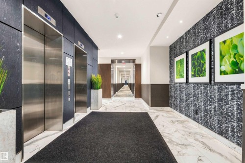 Dual stainless steel elevators with digital displays, recessed ceiling lighting, textured wall paneling, and marble-look flooring - #416 2510 109 St Nw, Edmonton, AB 