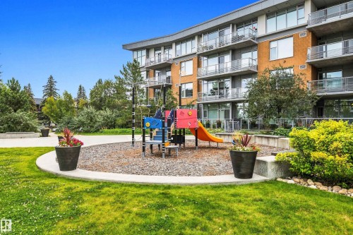 Manicured lawn with a curved concrete pathway and a colorful playground structure - #416 2510 109 St Nw, Edmonton, AB 