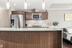 Stainless steel appliances, wood-finish cabinetry, recessed lighting, stone countertops, and a kitchen island with a sink - 