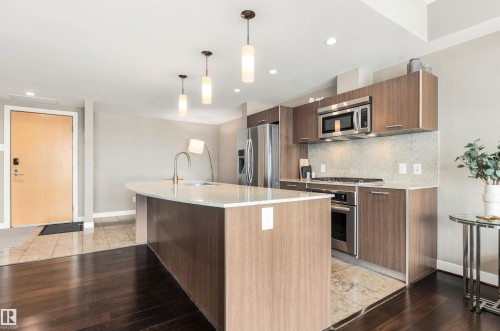 Kitchen with wood-finish cabinetry, stainless steel appliances, and a curved island with a white countertop - #416 2510 109 St Nw, Edmonton, AB 