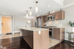 Kitchen with wood-finish cabinetry, stainless steel appliances, and a curved island with a white countertop - 