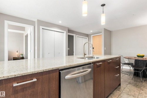 Kitchen island featuring a double basin sink, stainless steel dishwasher, and wood-finish cabinetry with silver hardware - #416 2510 109 St Nw, Edmonton, AB 