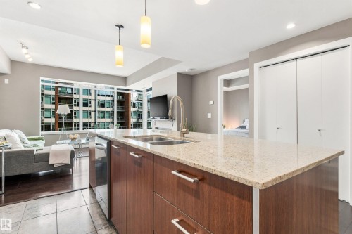 Kitchen island with a light-toned countertop, integrated double sink, and wood-finish cabinetry - #416 2510 109 St Nw, Edmonton, AB 