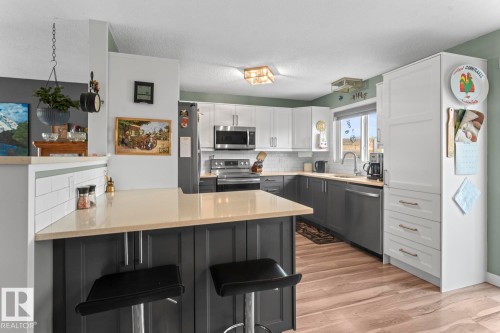 Kitchen featuring wood-finish flooring, two-tone cabinetry, stainless steel appliances, light-toned countertops, and a white subway tile backsplash - 1303 12 Street, Cold Lake, AB 