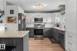 Modern kitchen featuring two-tone cabinetry, stainless steel appliances, a white subway tile backsplash, light-toned countertops, and wood-finish flooring - 