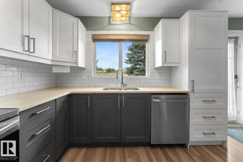 Kitchen featuring two-tone cabinetry, wood-finish flooring, a stainless steel dishwasher, white subway tile backsplash, and a window above the sink - 1303 12 Street, Cold Lake, AB 