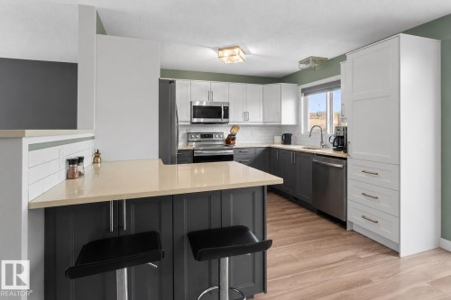 Kitchen featuring light-tone countertops, stainless steel appliances, two-tone cabinetry, wood-finish flooring, and a white subway tile backsplash - 1303 12 Street, Cold Lake, AB 