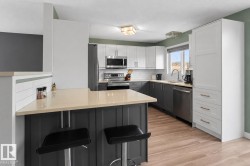 Kitchen featuring light-tone countertops, stainless steel appliances, two-tone cabinetry, wood-finish flooring, and a white subway tile backsplash - 