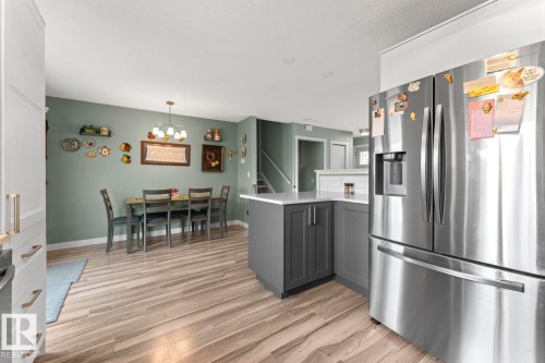 Open-concept dining area featuring wood-finish flooring, a contemporary chandelier, and a stainless steel refrigerator - 1303 12 Street, Cold Lake, AB 