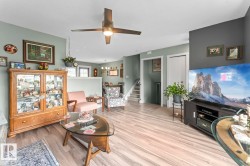 Spacious living area featuring light wood-finish flooring, a contemporary ceiling fan with integrated lighting, and a defined accent wall - 