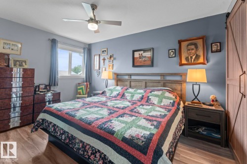 Spacious room featuring wood-finish flooring, a window with natural light, a ceiling fan with integrated lighting, and a sliding barn door - 1303 12 Street, Cold Lake, AB 