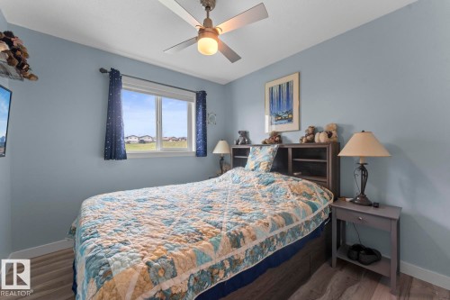 Light-filled room featuring wood-finish flooring, a ceiling fan with integrated lighting, a window with exterior views, and a headboard with integrated shelving - 1303 12 Street, Cold Lake, AB 