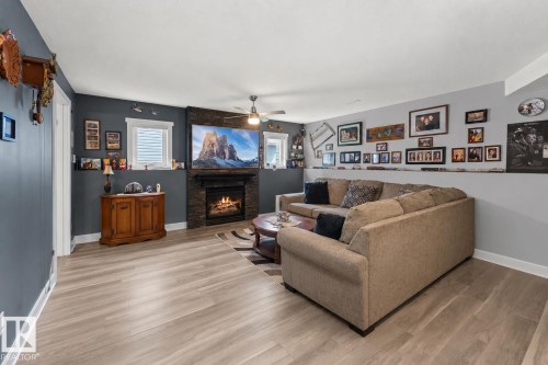 Living space featuring wood-finish flooring, a stone-clad fireplace with a gas insert, and a ceiling fan - 1303 12 Street, Cold Lake, AB 