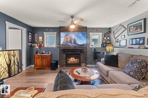 Living area featuring a stone-faced fireplace with hearth, wood-finish flooring, and a ceiling fan with integrated lighting - 1303 12 Street, Cold Lake, AB 