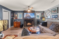 Living area featuring a stone-faced fireplace with hearth, wood-finish flooring, and a ceiling fan with integrated lighting - 