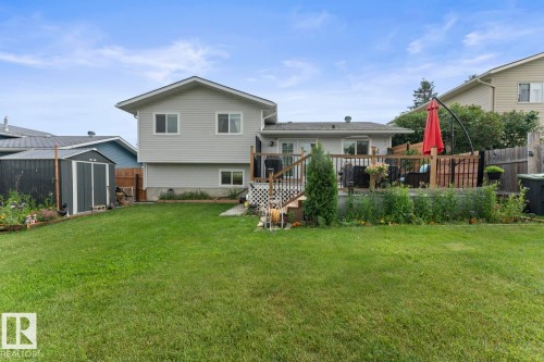 Expansive backyard featuring a large green lawn, an elevated wood deck with railing, sliding glass doors, and a detached storage shed - 1303 12 Street, Cold Lake, AB 