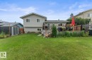 Expansive backyard featuring a large green lawn, an elevated wood deck with railing, sliding glass doors, and a detached storage shed - 1303 12 Street, Cold Lake, AB 
