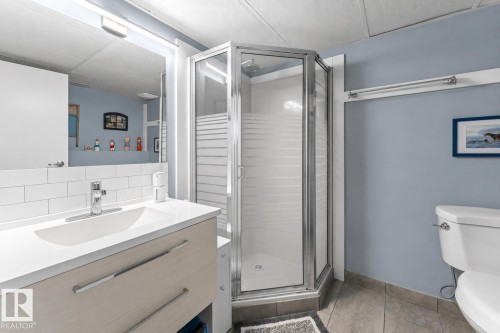 Bathroom featuring a corner shower with a glass enclosure, a vanity with a white countertop and integrated sink, a large wall-mounted mirror, and a toilet - 1303 12 Street, Cold Lake, AB 
