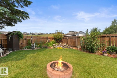 Expansive backyard featuring a central fire pit, established wood fencing, a dedicated garden bed, and two detached storage sheds - 1303 12 Street, Cold Lake, AB 
