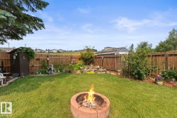 Expansive backyard featuring a central fire pit, established wood fencing, a dedicated garden bed, and two detached storage sheds - 