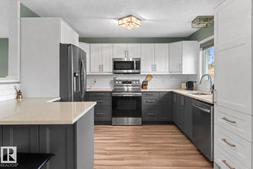 Modern kitchen featuring two-tone cabinetry, stainless steel appliances, light-toned countertops, subway tile backsplash, and wood-finish flooring - 1303 12 Street, Cold Lake, AB 