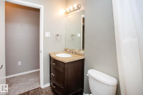 Bathroom featuring a dark wood vanity with a stone countertop, an undermount sink, and a wall-mounted light fixture - #8 15431 93 Av Nw, Edmonton, AB 