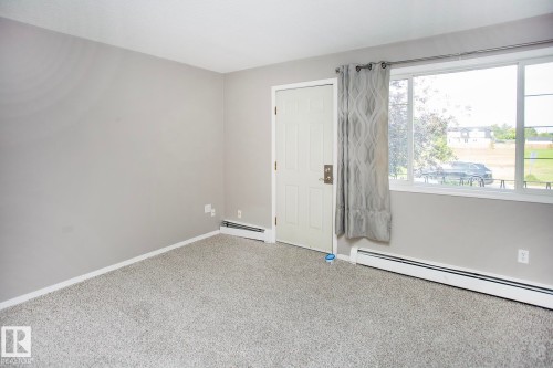 Neutral wall paint, plush carpet flooring, white paneled door, and large window with white trim - #8 15431 93 Av Nw, Edmonton, AB 