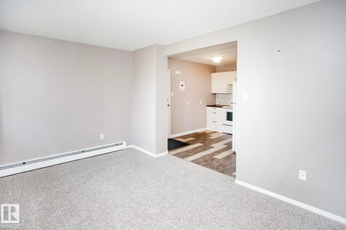 Neutral wall paint, light-colored carpeting, white baseboards, and a recessed kitchen area with white cabinetry - #8 15431 93 Av Nw, Edmonton, AB 