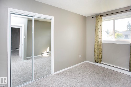 Wall-to-wall carpeting, neutral wall color, white trim, mirrored closet doors, and window with baseboard heating - #8 15431 93 Av Nw, Edmonton, AB 