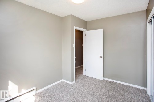 Neutral tone wall finish, textured carpet flooring, white trim, and a flush-mount ceiling light fixture - #8 15431 93 Av Nw, Edmonton, AB 