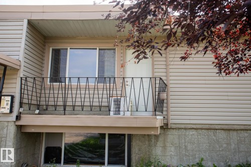 Exterior featuring horizontal siding, a balcony with a geometric metal railing, and ground-level windows - #8 15431 93 Av Nw, Edmonton, AB 