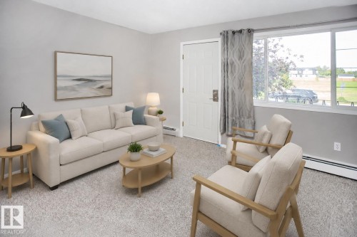 Carpeted living space with neutral wall tones and ample natural light from a large window. VIRTUALLY STAGED - #8 15431 93 Av Nw, Edmonton, AB 