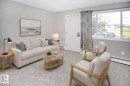 Carpeted living space with neutral wall tones and ample natural light from a large window. VIRTUALLY STAGED - #8 15431 93 Av Nw, Edmonton, AB 