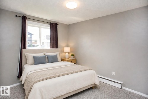 Wall-to-wall carpeting with light-colored walls and a window offering natural light. VIRTUALLY STAGED - #8 15431 93 Av Nw, Edmonton, AB 