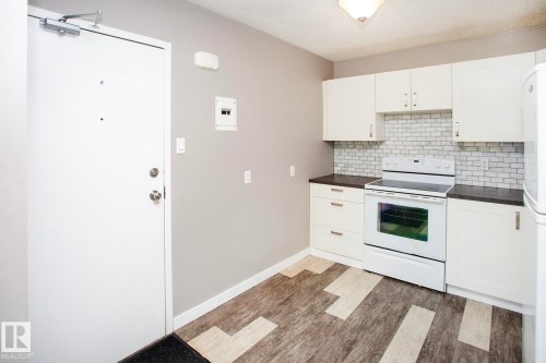 White cabinetry with brushed nickel hardware, dark countertops, a white subway tile backsplash, and a white electric range.  VIRTUALLY STAGED - #8 15431 93 Av Nw, Edmonton, AB 