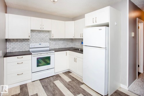 White cabinetry with modern hardware, dark countertops, a white subway tile backsplash, white electric range, and wood-finish flooring - #8 15431 93 Av Nw, Edmonton, AB 