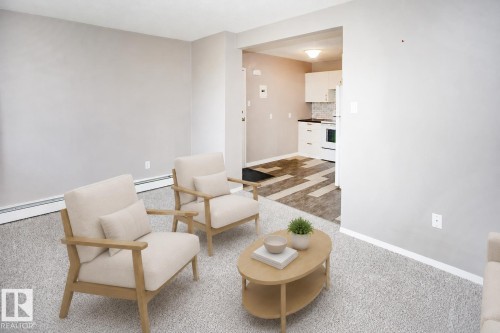 Carpeted living area with light gray walls, an open archway, and wood-finish flooring in the adjacent kitchen. VIRTUALLY STAGED - #8 15431 93 Av Nw, Edmonton, AB 