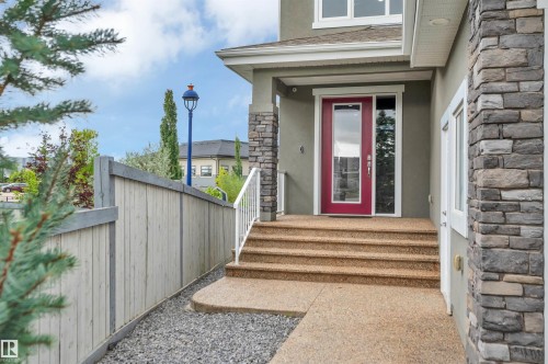Stone veneer exterior accents, vibrant red entry door with glass panel, white railing, exposed aggregate concrete steps, and a wooden privacy fence - 9054 24 Avenue Sw, Edmonton, AB 