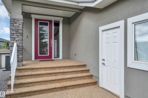 Stone veneer column accents a vibrant entry door with a full-length glass panel, complemented by a white-framed sidelight - 9054 24 Avenue Sw, Edmonton, AB 